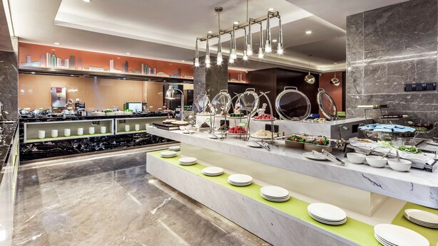 Un bufé moderno de hotel con encimeras de mármol, diversas opciones de comida e iluminación contemporánea.