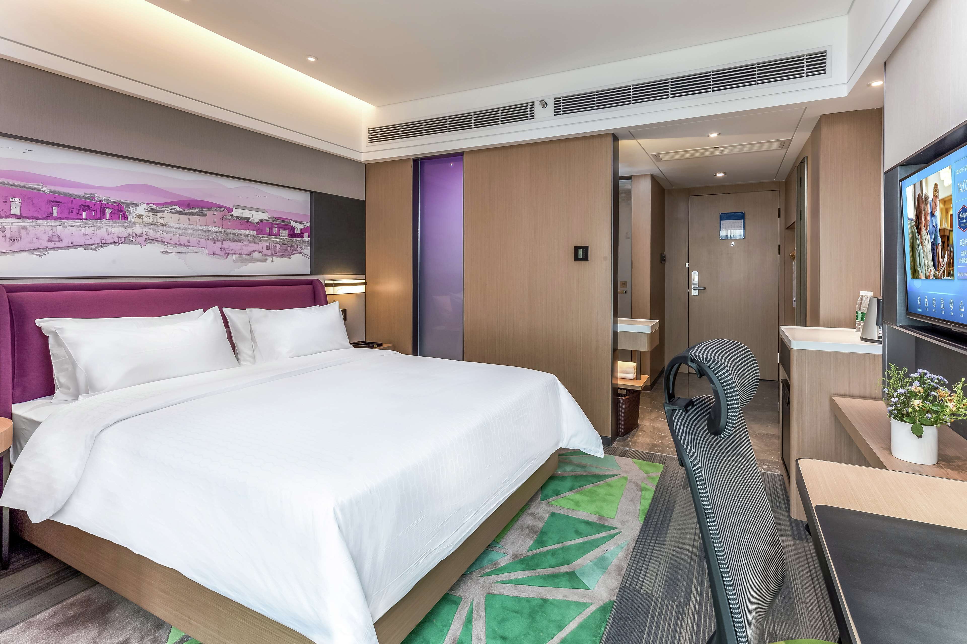 Ein Hotelzimmer mit einem großen Bett, einem Schreibtisch mit Stuhl, einem Fernseher und einem durchgegangenen Tür erkennbaren Badezimmer.