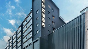 Un hotel moderno con un letrero llamativo en caracteres chinos, ventanas amplias y una zona de entrada bien iluminada.