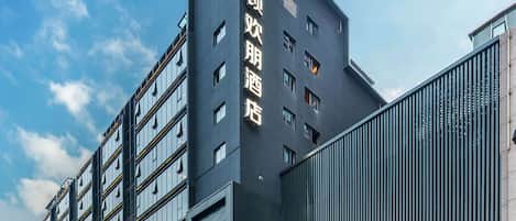 A modern hotel building with a prominent sign in Chinese characters, large windows, and a well-lit entrance area.