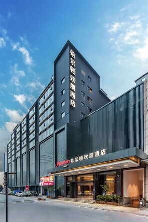 Ein modernes Hotelgebäude mit einer auffälligen Beschilderung in chinesischen Schriftzeichen, großen Fenstern und einem gut beleuchteten Eingangsbereich.