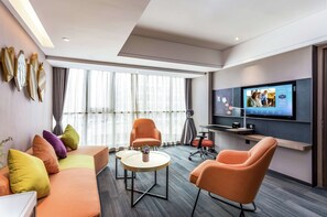 A modern hotel room with a sofa, two armchairs, a coffee table, and a television mounted on the wall.