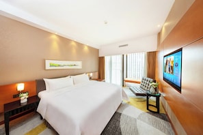 Habitación de hotel con una cama grande, un escritorio, una silla, un televisor de pantalla plana y una ventana con cortinas.