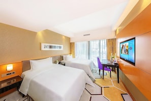 Habitación de hotel con dos camas, un escritorio con silla, televisión y ventana con cortinas.