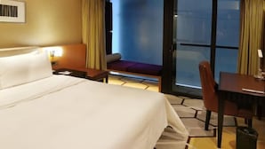 A hotel room with a bed, a desk, a chair, and a view through a glass door.