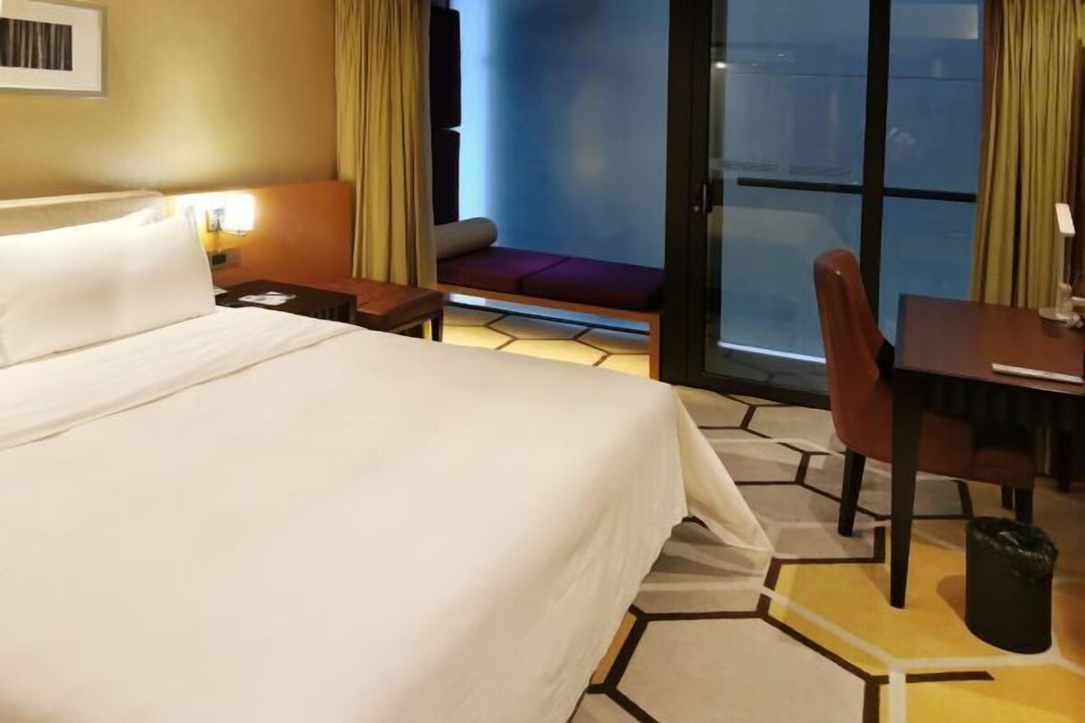 Habitación de hotel con cama, escritorio, silla y vistas a través de un ventanal.