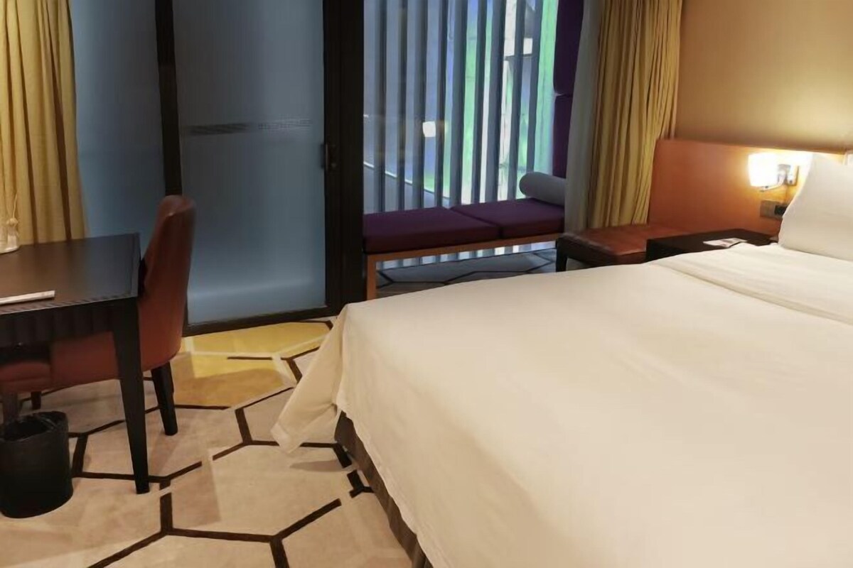 Habitación de hotel con cama, escritorio y silla. Cuenta con una ventana con cortinas y vistas al exterior.