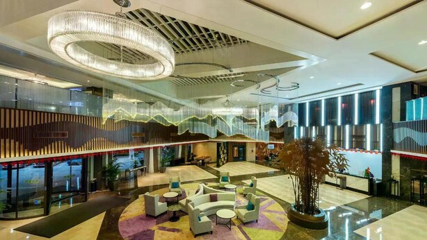 A hotel lobby with a central seating area, a large chandelier, and a glass partition with a view.