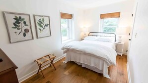 A bedroom with a bed, two bedside tables, a small wooden stool, and two framed botanical illustrations on the wall. - Historical Hotel, Main Street Blowing Rock (Blowing Rock)