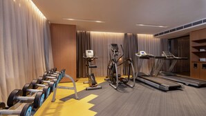 Een hotelgymzaal met fitnessapparatuur, waaronder gewichten, een elliptische trainer en loopbanden.