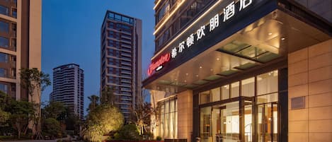 A modern hotel with a prominent sign, large windows, and a well-lit entrance.