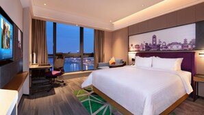 Een hotelkamer met een groot bed, een bureau met stoel, een televisie en uitzicht op de stad.