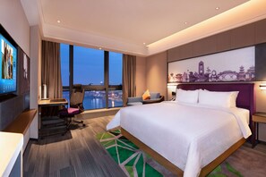 A hotel room with a large bed, a desk with a chair, a TV, and a city view. - Hampton BY Hilton Chengdu Wciec (CHENGDU)
