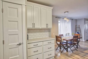 A kitchen with white cabinets, a dining table with chairs, and a hanging light fixture.
