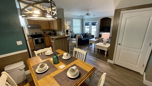 A dining area with a wooden table set for four, a kitchen with modern appliances, and a living room with a sofa and TV. - Lake view gorgeous condo 3bd - 10 min from Disney (Kissimmee)