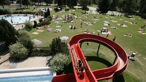 A water slide at a park with a pool, grassy areas, and people relaxing. - Modern Comfortable Apartment with Balcony and Garage. Great Location for Skiing. (Samoëns)