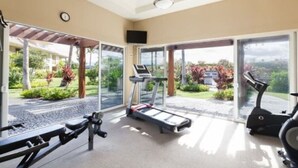 A gym with exercise equipment, large sliding glass doors, and a view of a landscaped garden. - ‘26 Special! 2Bed/2Bath—BBQ/Hilton Pass/Walkable! (WAIKOLOA)