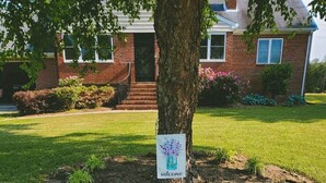 Una casa de ladrillo con un letrero de bienvenida en un árbol del jardín delantero.