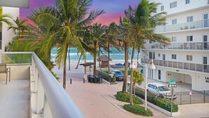 Un balcón con vistas a una playa, palmeras y un edificio con balcones.