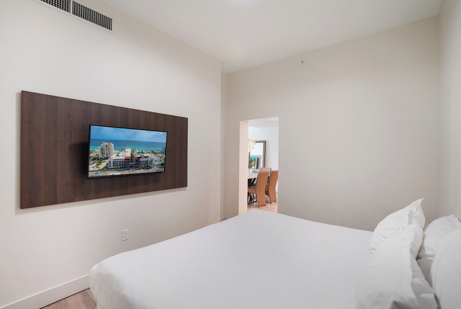 A hotel room with a bed, a mounted TV, and a view of the dining area.