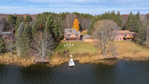 A large house with a deck and a boat docked in a lake surrounded by trees. - Kenny Lodge (Cable)