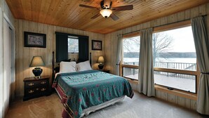 A bedroom with a bed, two bedside tables, a ceiling fan, and a large window with curtains. - Kenny Lodge (Cable)