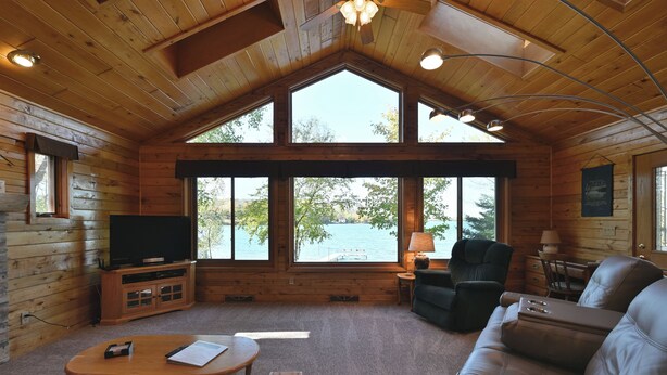 Een chalet met een groot raam, een televisie, een leren bank en een houten bijzettafeltje.