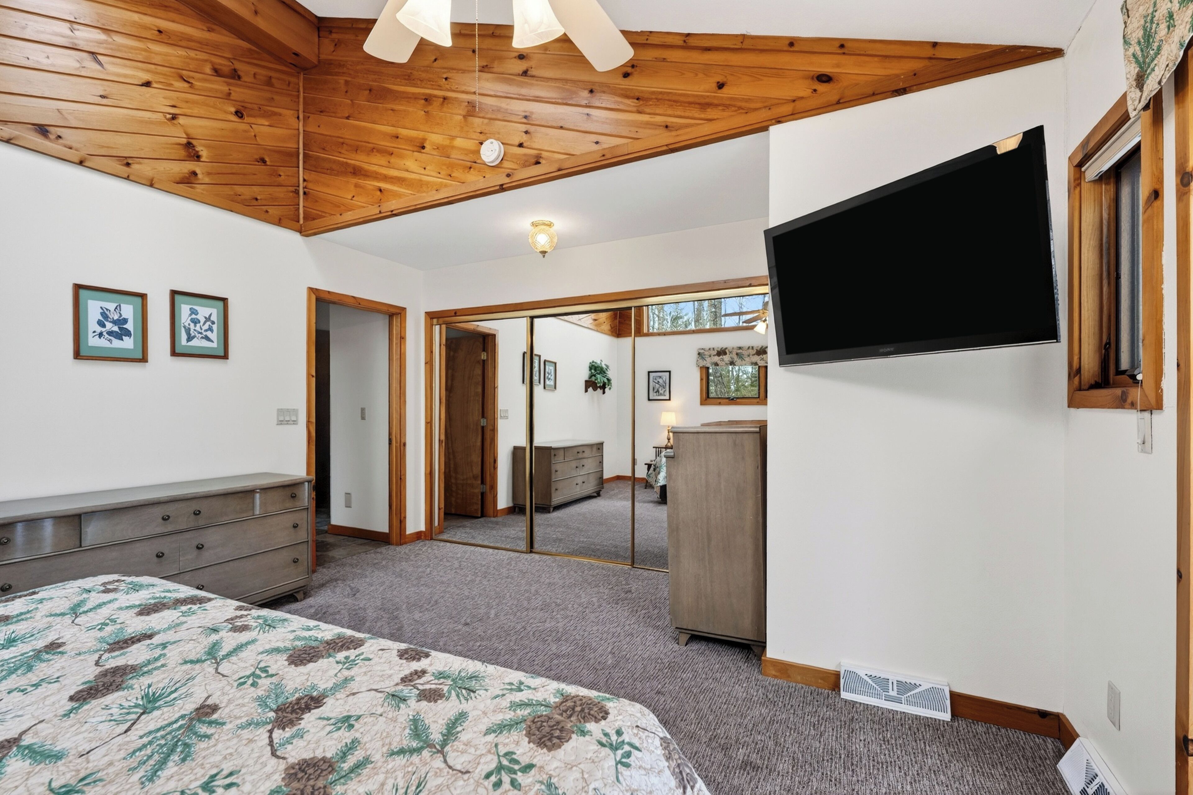 A bedroom with a bed, dresser, mirror, and a TV mounted on the wall.