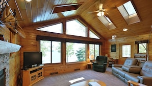 Een gezellig cabin interieur met houten inrichting, grote ramen, een televisie, een bank en een open haard.