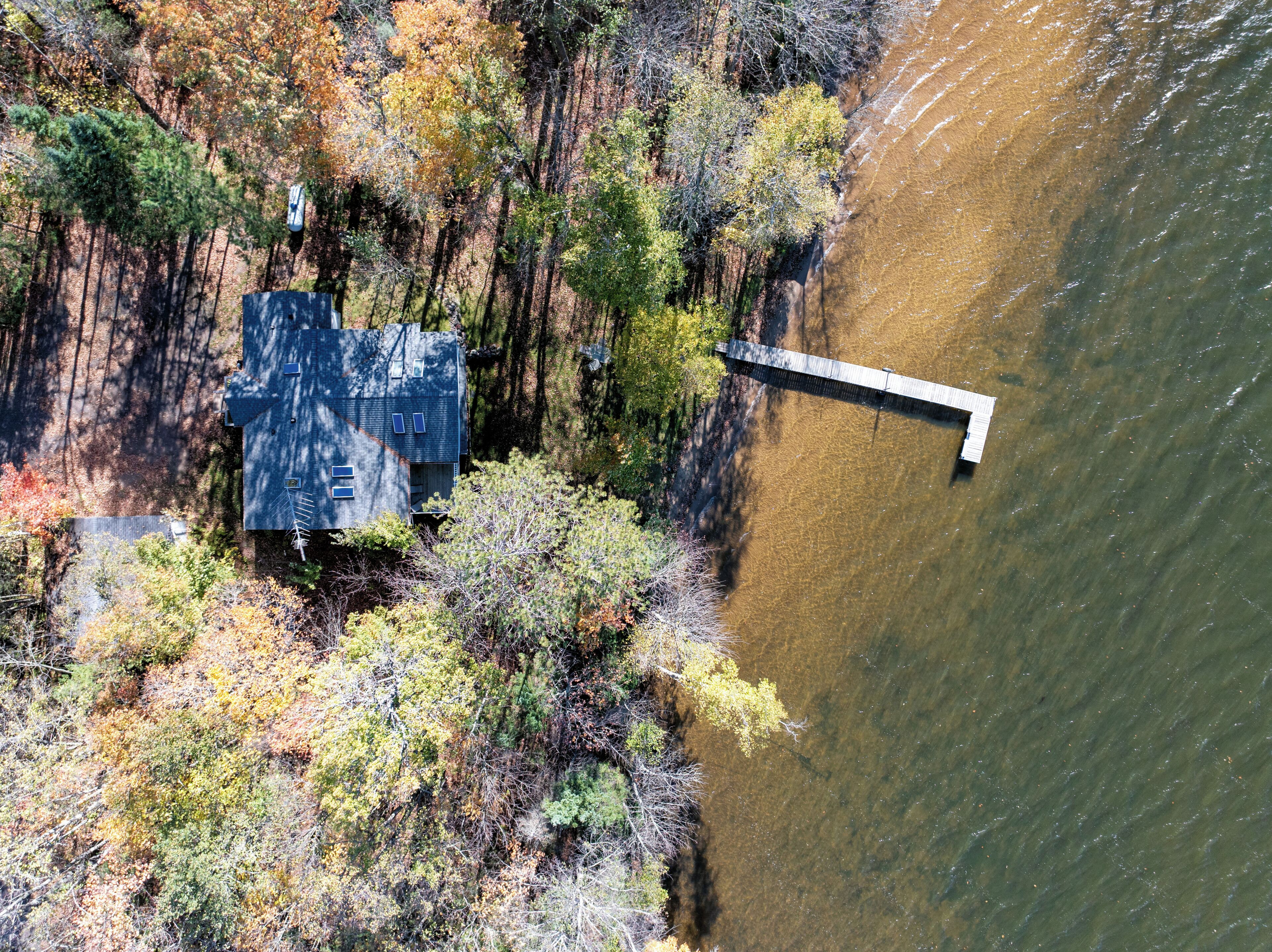 Vue aérienne d’une maison avec un quai s’étendant dans une rivière, le tout entouré d’une végétation luxuriante.