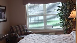 A bedroom with a bed, a chair, a window with blinds, and a plant.