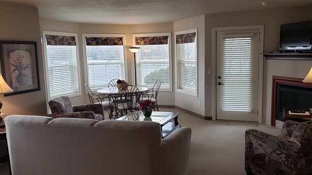 A living room with a sofa, patterned chairs, a dining table with chairs, a fireplace, and a television on a stand.