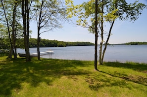 A lakeside view with a dock extending into the water, surrounded by trees and grassy areas.