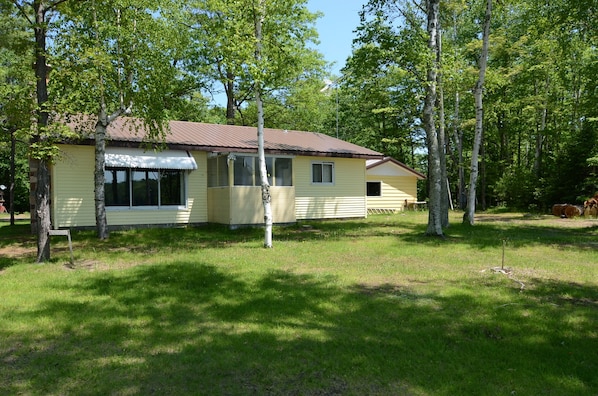 A yellow single-story house with a brown roof, surrounded by trees and grass.