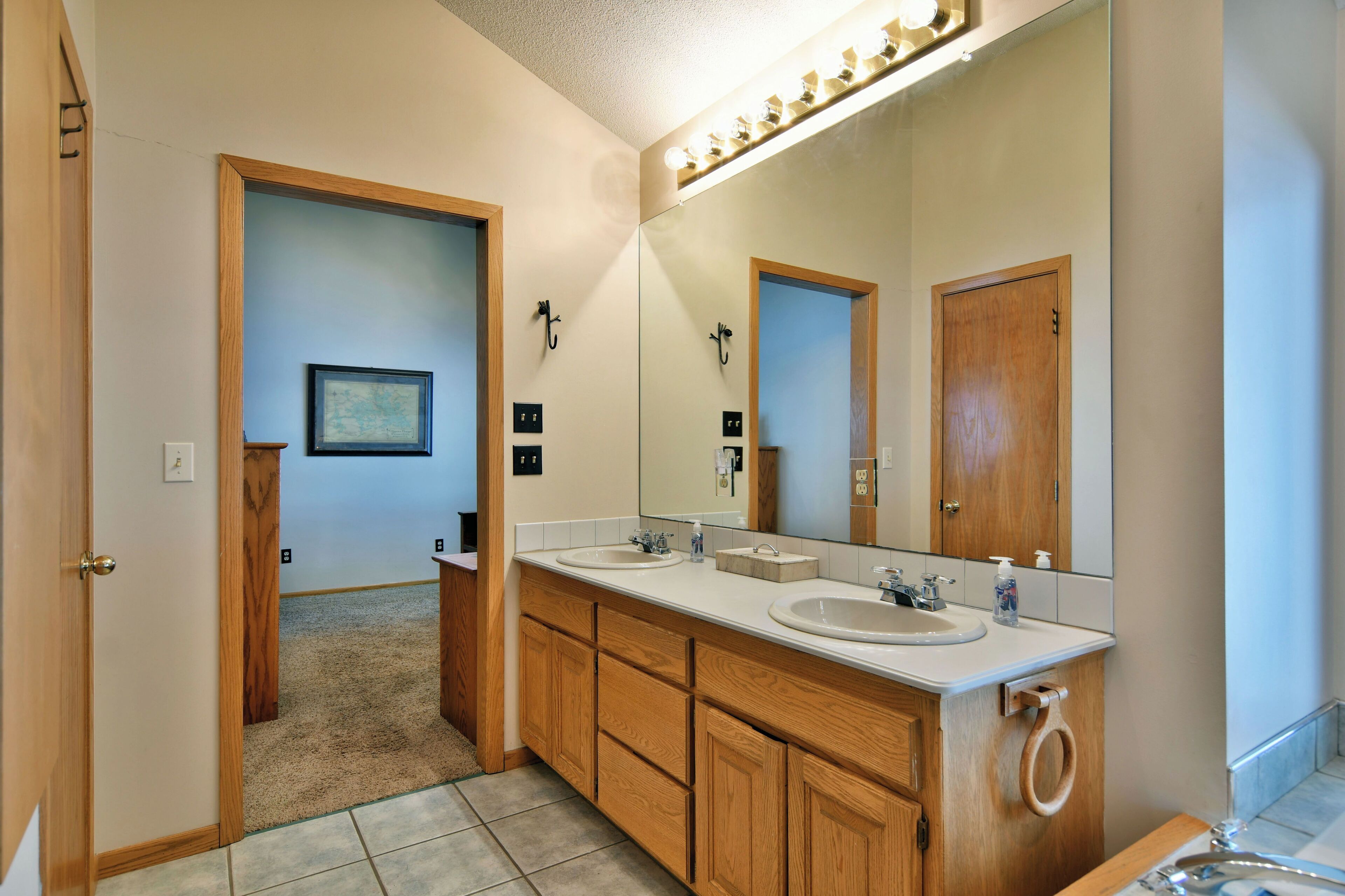 A modern bathroom with wooden cabinetry, two sinks, a large mirror, and a towel ring.