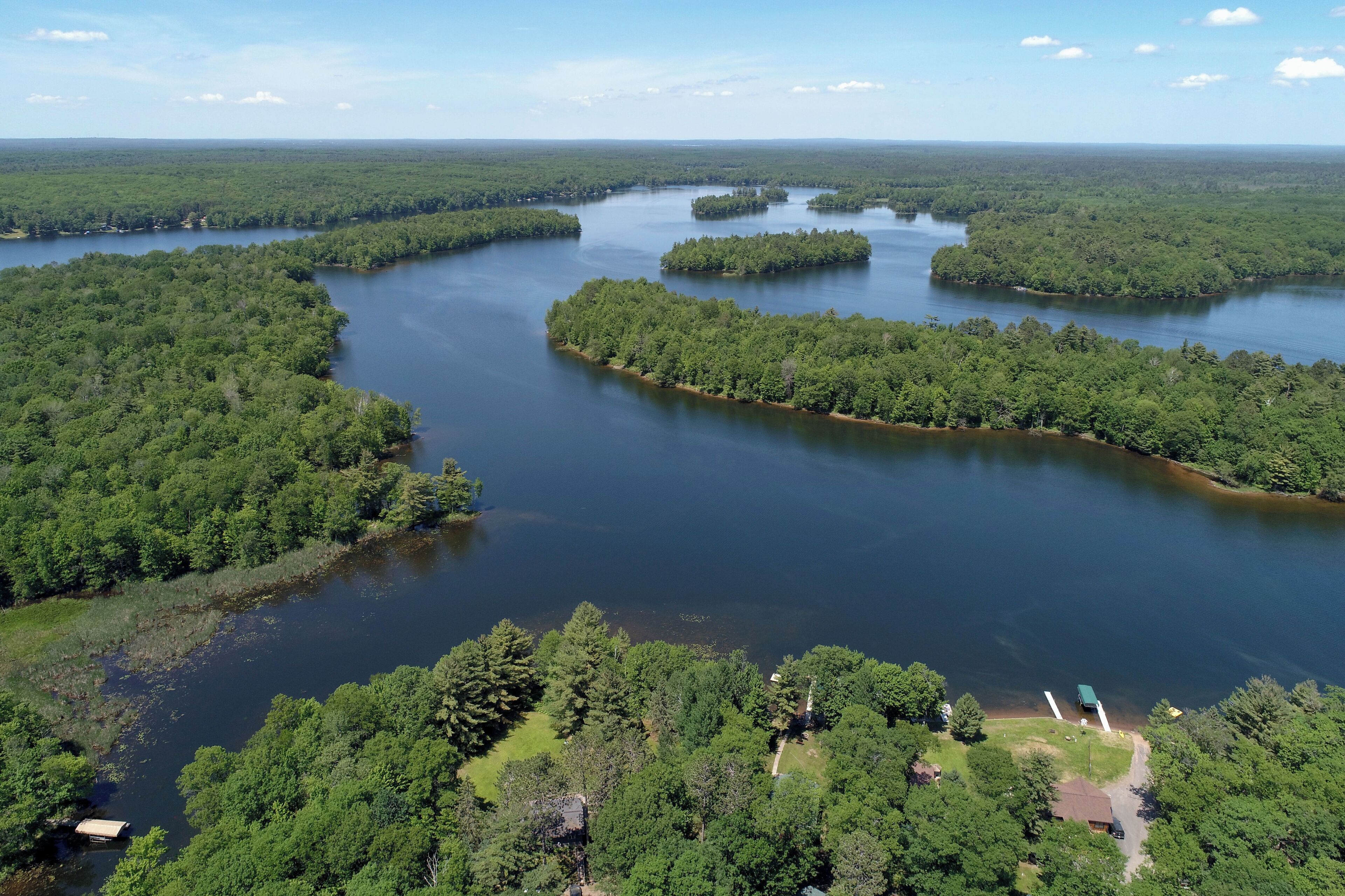 Une vue aérienne d’une zone boisée avec un lac, entourée d’une végétation luxuriante et de quelques bâtiments visibles.