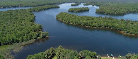 Une vue aérienne d’une zone boisée avec un lac, entourée d’une végétation luxuriante et de quelques bâtiments visibles.