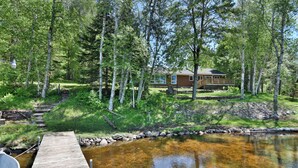 A wooden dock leading to a clear pond with a cabin in the background surrounded by trees. - Butler's Bay Teal Lake Cabin (Hayward)