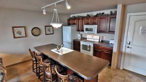 A kitchen with a central island, wooden cabinets, a refrigerator, microwave, and a stove. - Unit 312 1 BD/ 1 BA Condo (Birchwood)
