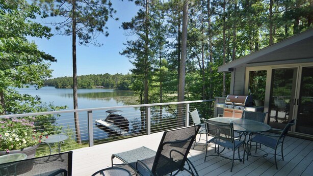 Um deck com móveis de exterior, churrasqueira e vista para um lago.