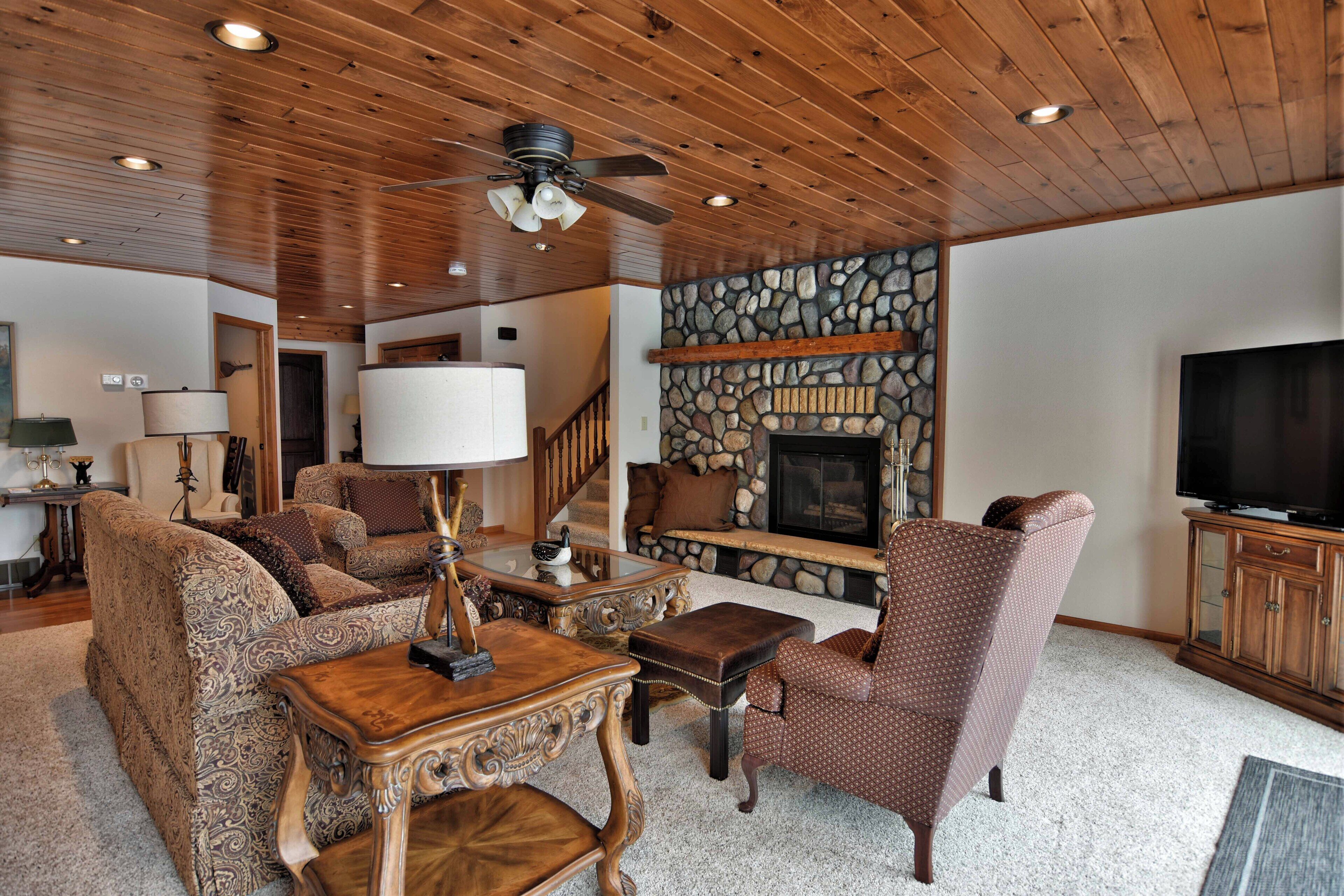A living room with a stone fireplace, wooden ceiling, and a television cabinet.