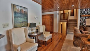 A spacious living room with a wooden ceiling, a stone wall, and a staircase leading to an upper level. - Peace of Mind on Namakagon (Cable)