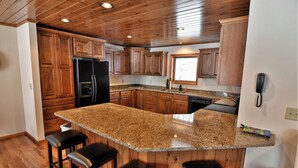 A kitchen with wooden cabinets, a granite countertop, and a built-in island with bar stools. - Peace of Mind on Namakagon (Cable)