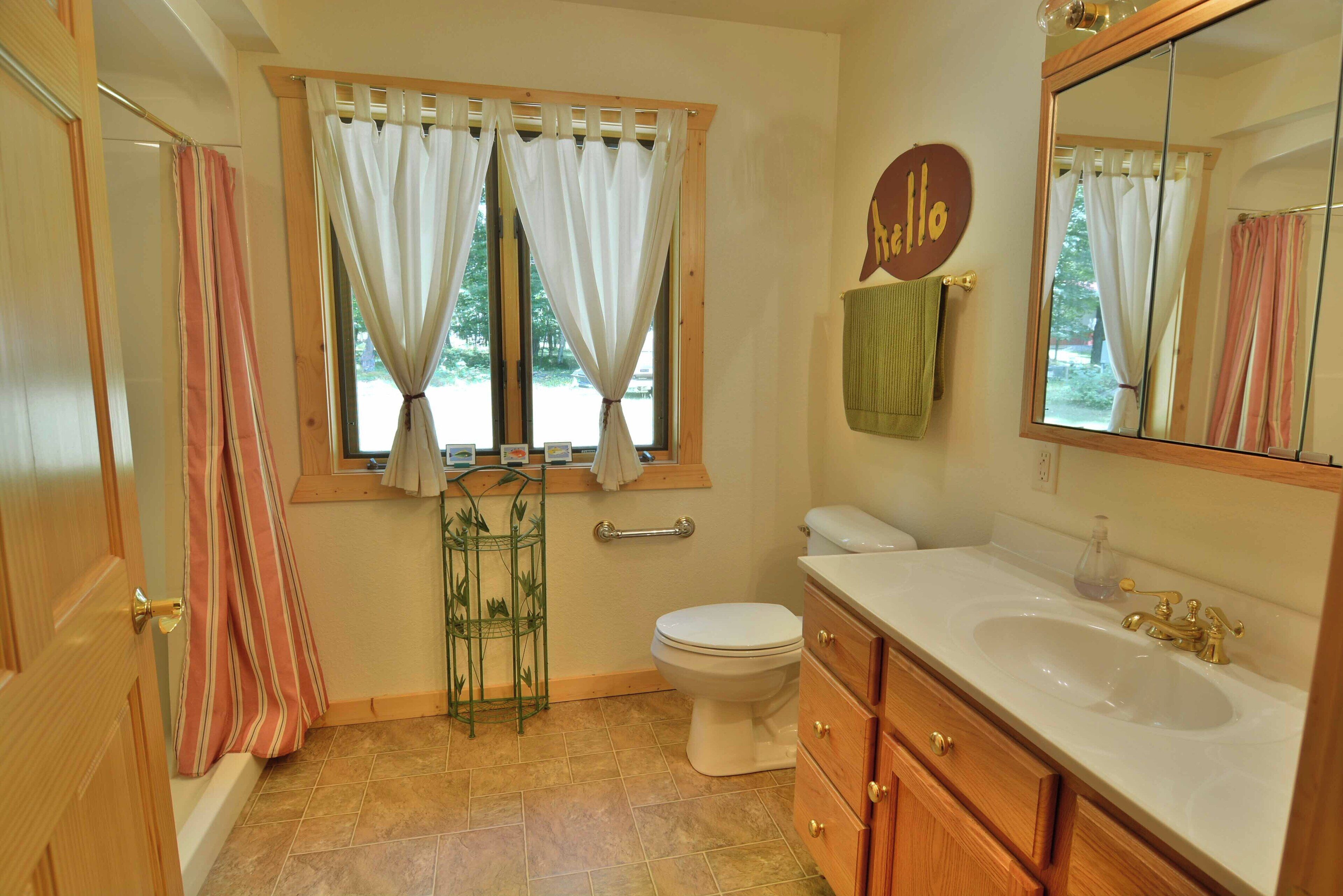 A bathroom with a toilet, sink, and shower. There is a window with curtains and a towel rack.