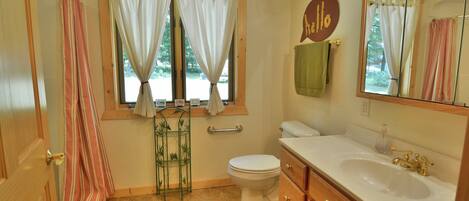 A bathroom with a toilet, sink, and shower. There is a window with curtains and a towel rack.