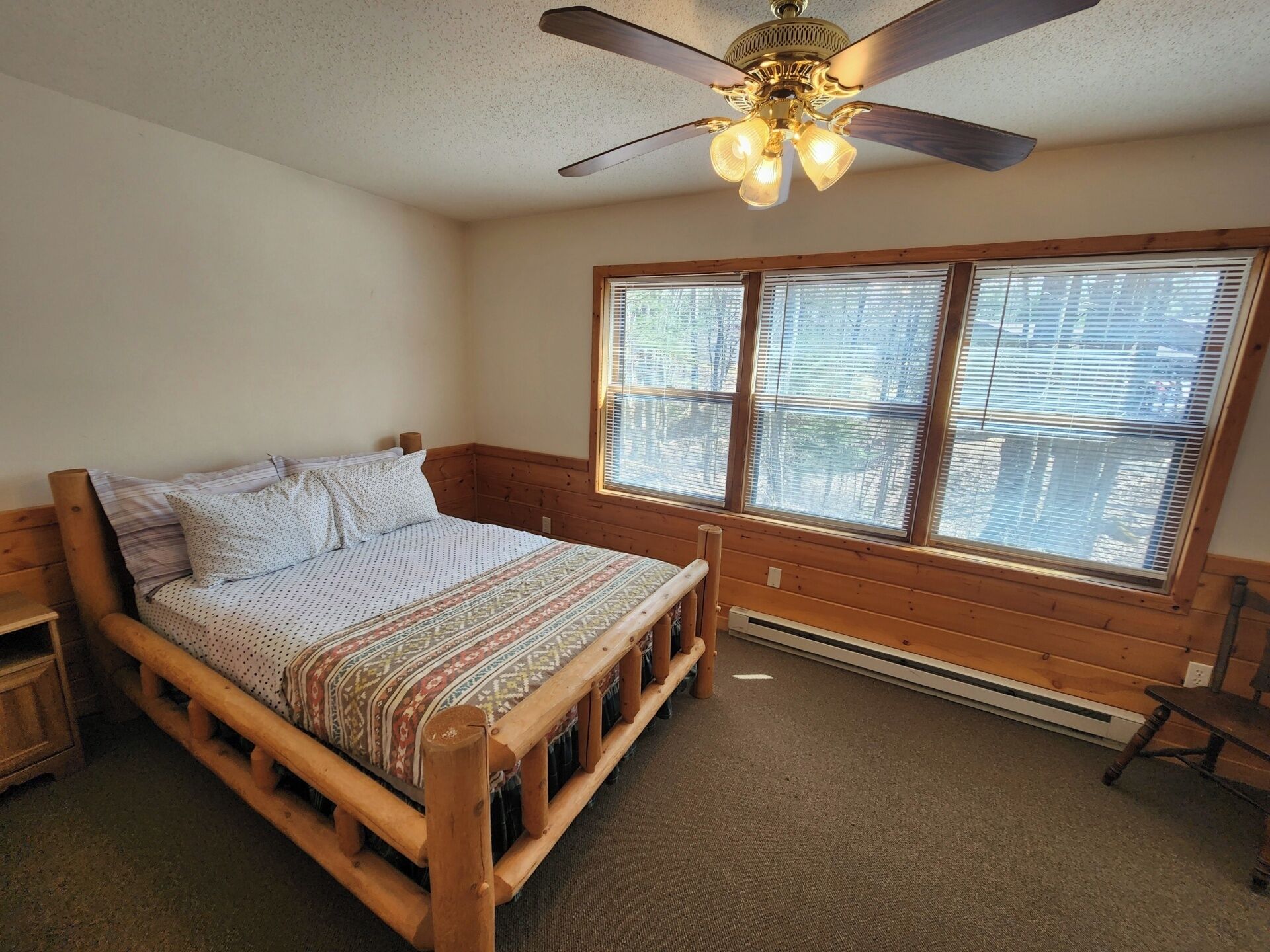 A bedroom with a wooden bed, a ceiling fan, and a large window with blinds.
