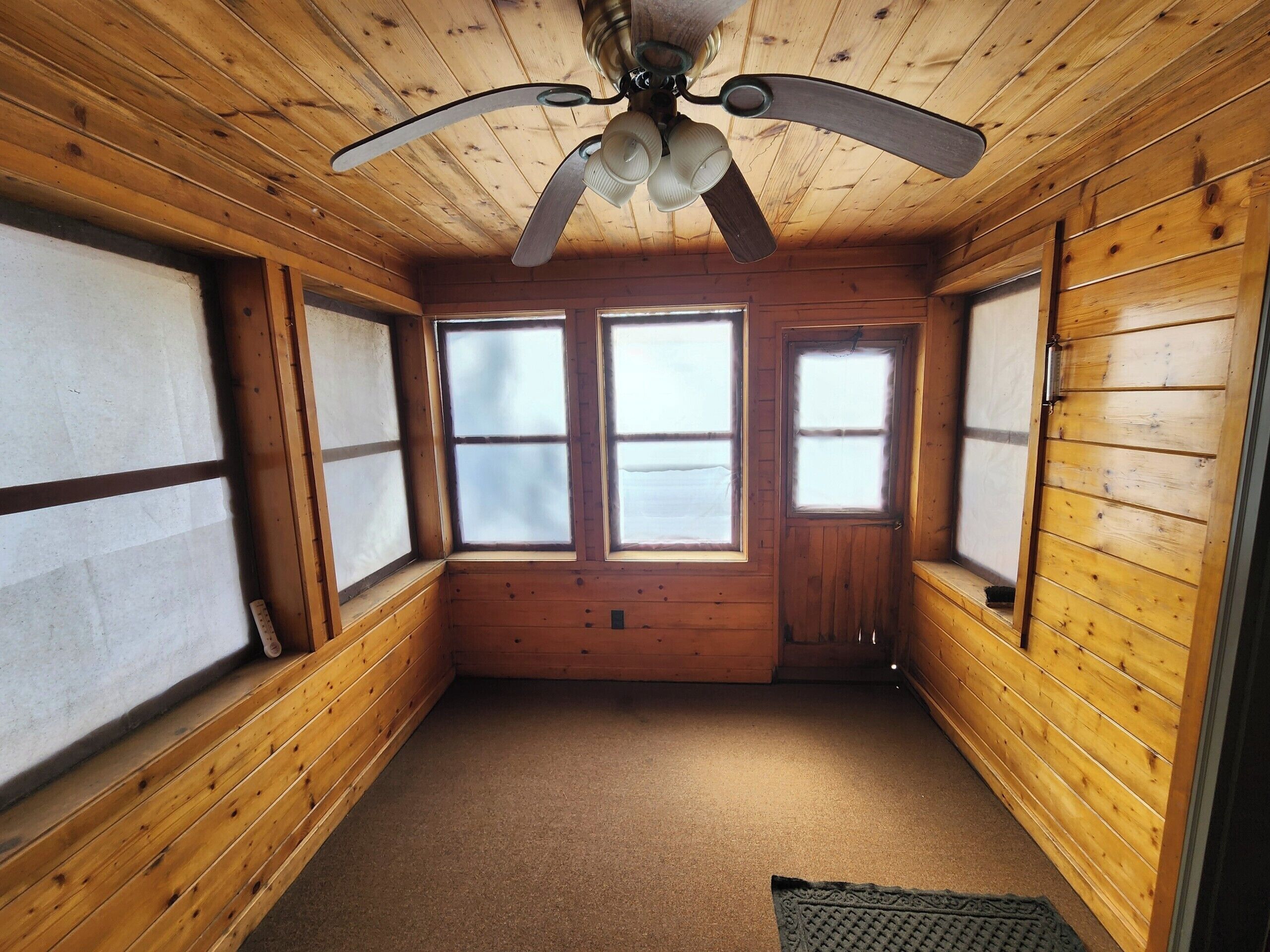 Une cabane aux murs en bois, dotée d’un ventilateur de plafond et de trois fenêtres.