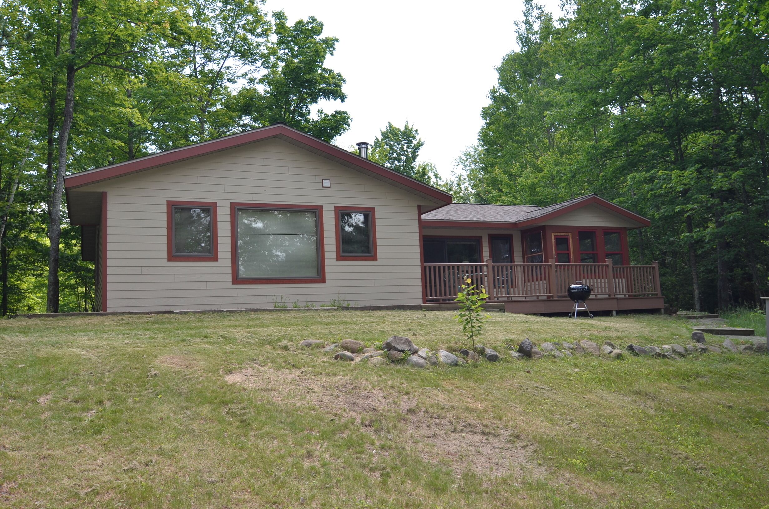 A two-story house with a front deck, a small garden area with rocks, and a grill.
