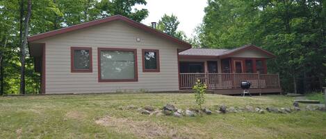 A two-story house with a front deck, a small garden area with rocks, and a grill.