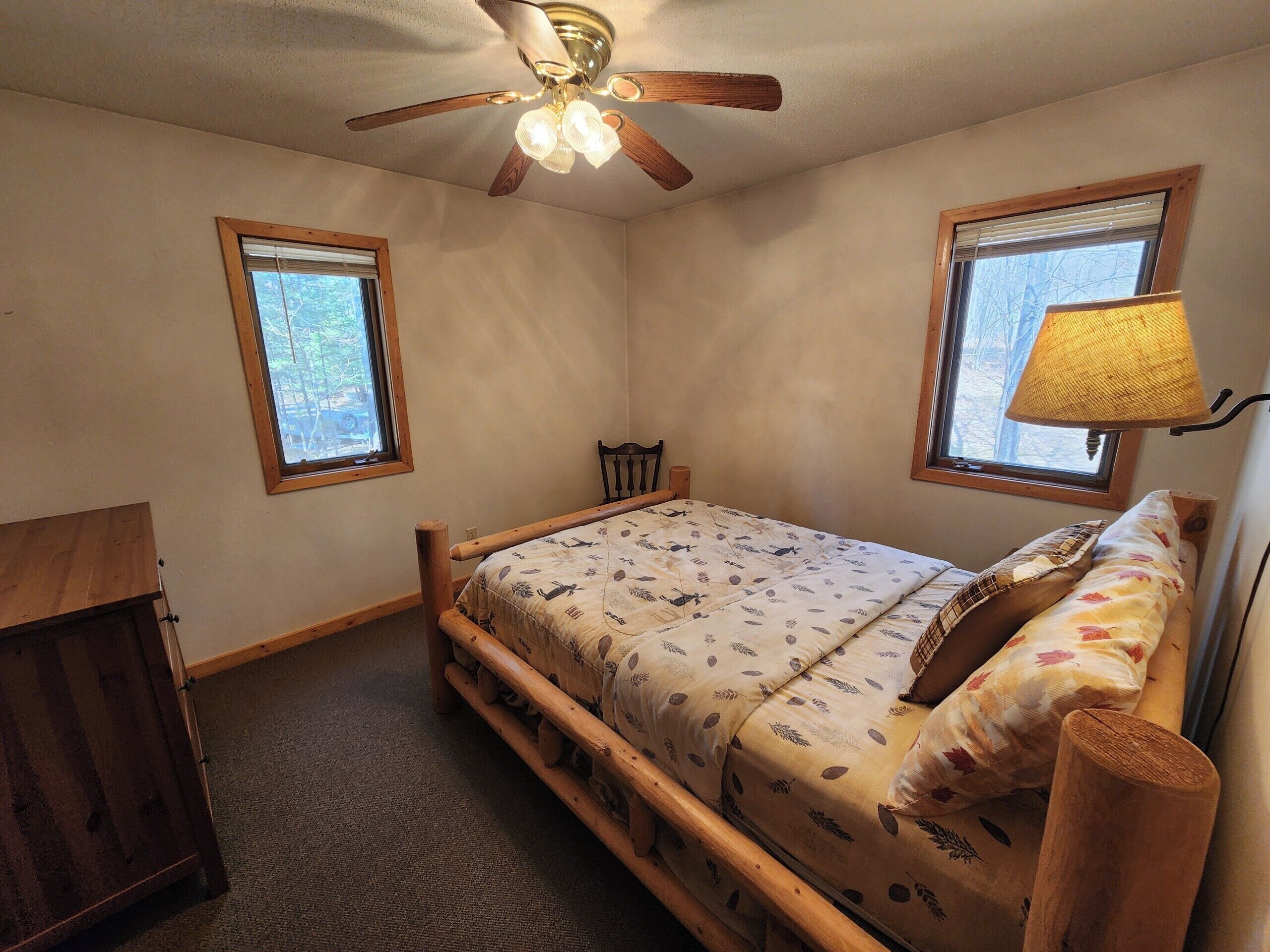 A bedroom with a wooden bed, two windows, a ceiling fan, and a lamp.